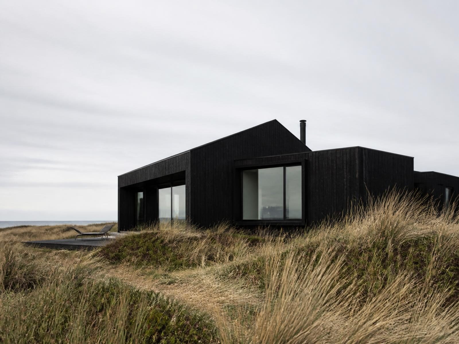 Black timber-clad house set low among coastal dune grass